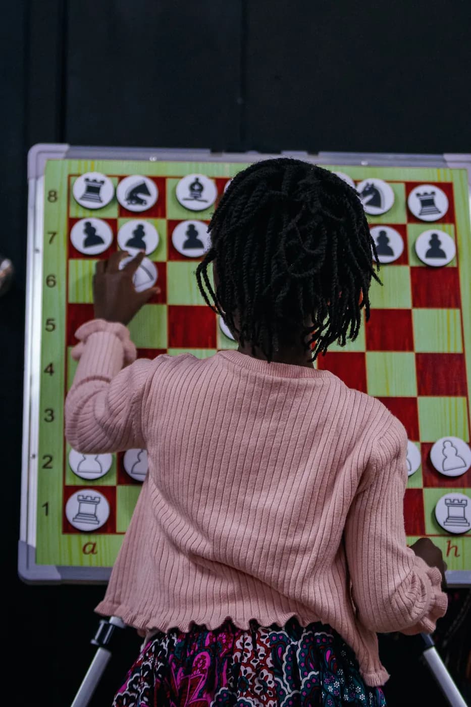A young girl in a pink cardigan moves a piece on a big magnetic demonstration board