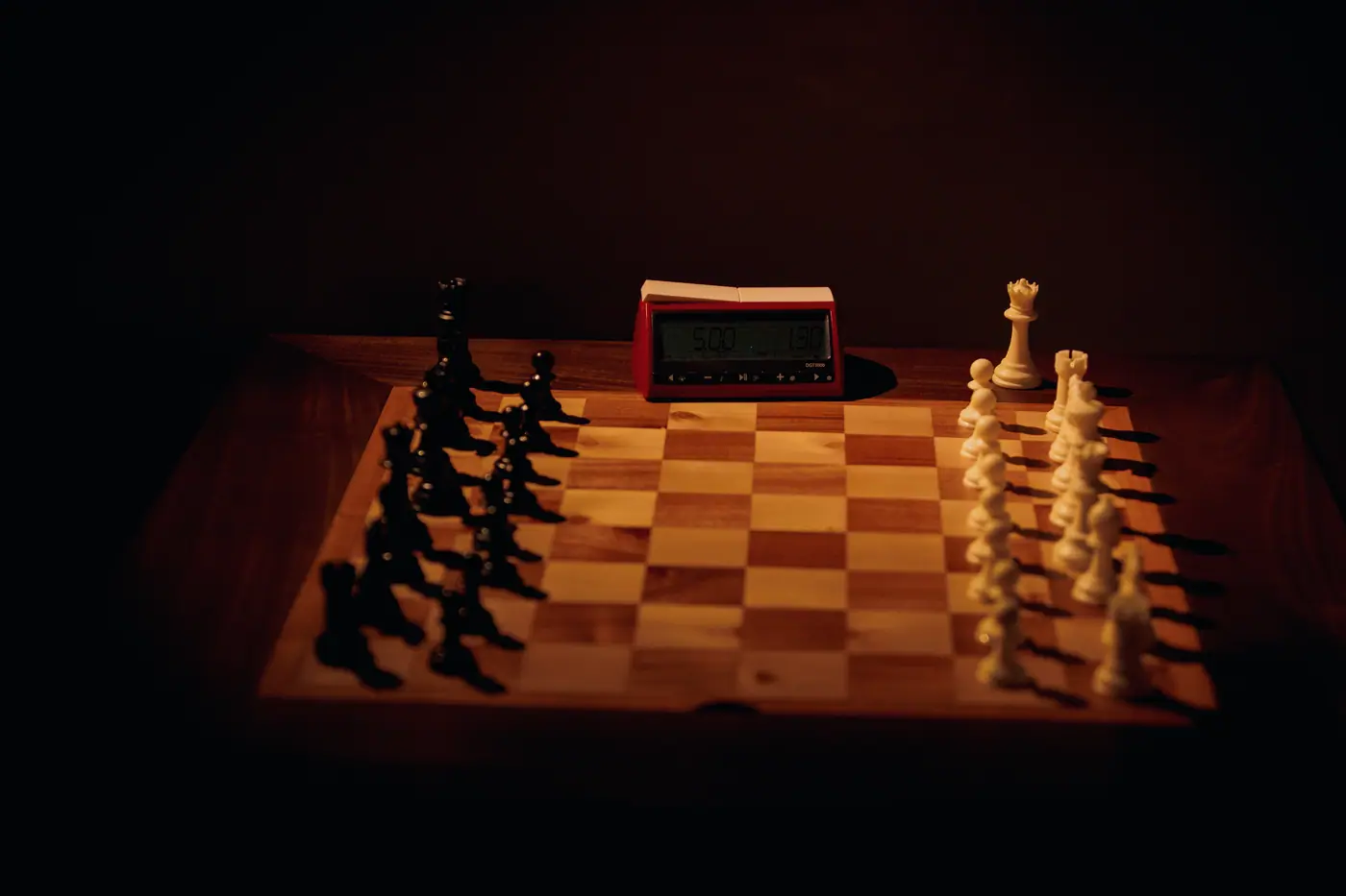A wooden chessboard and clock lit warm orange on a dark table
