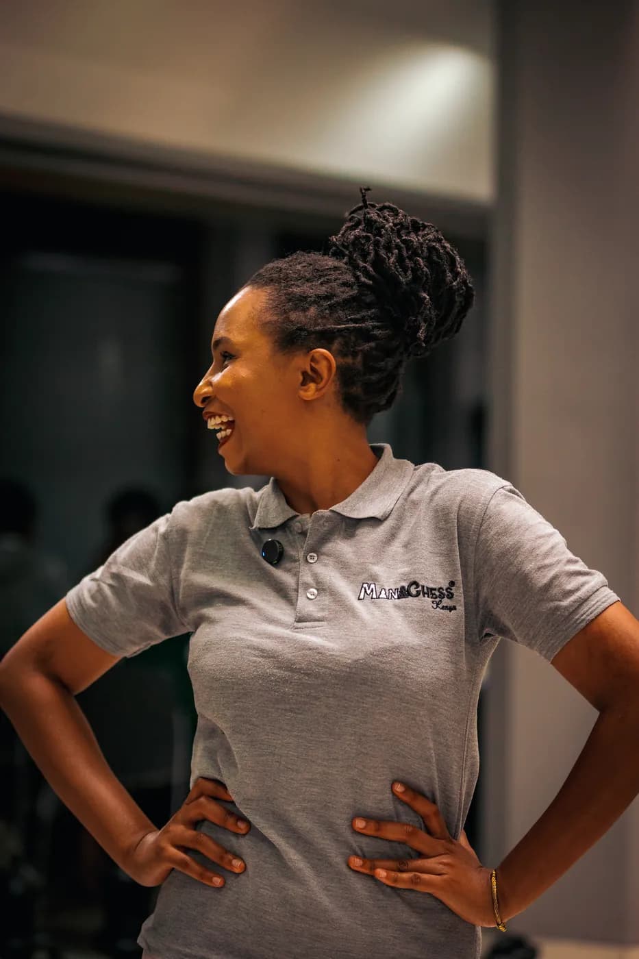 A woman in a grey club polo laughs with her hands on her hips