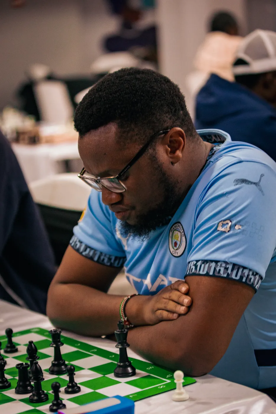 A player in a light blue football jersey and glasses folds his arms over a green board