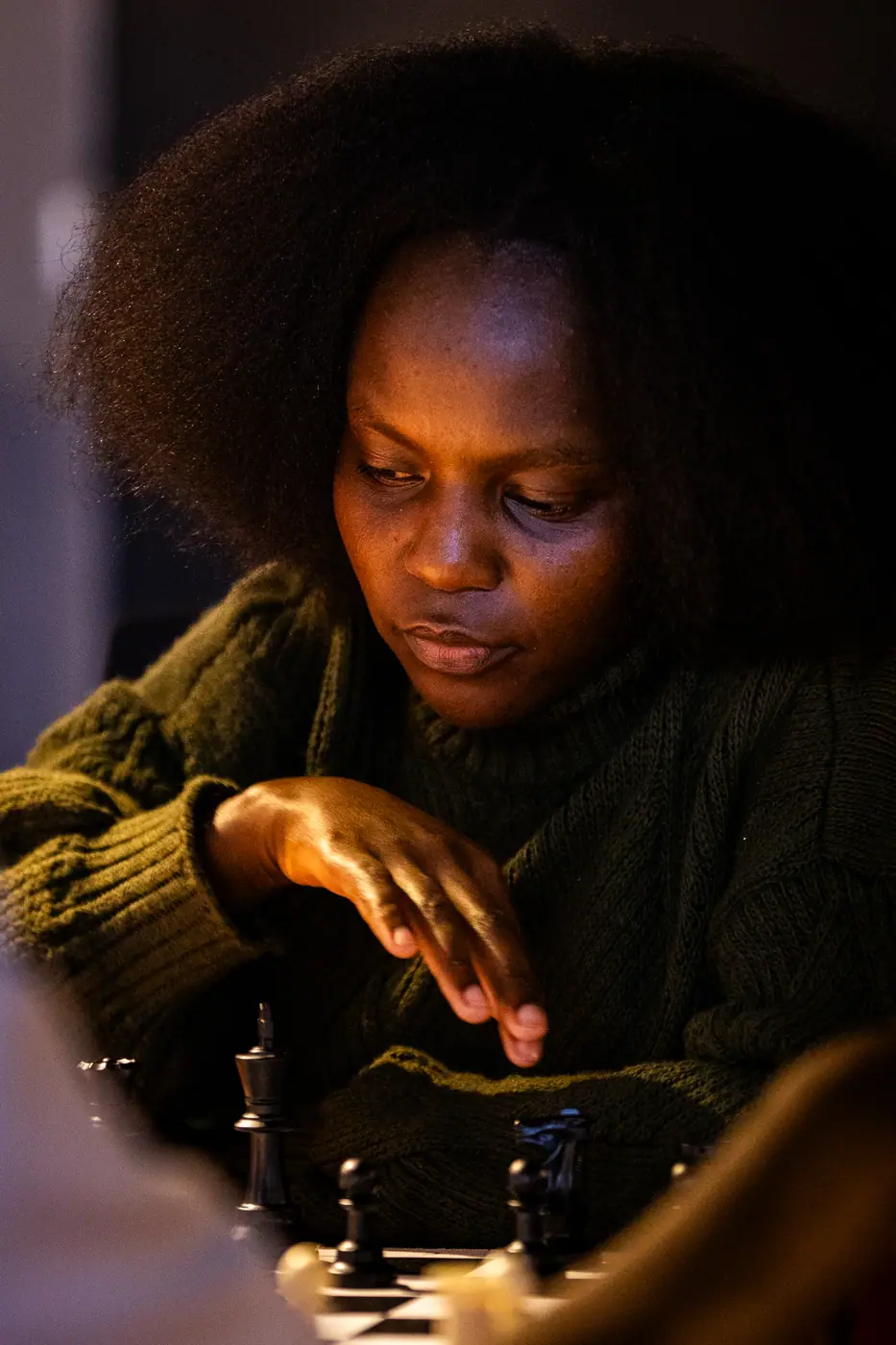 A player with an afro, in a dark knit sweater, concentrates on her move in warm, low light