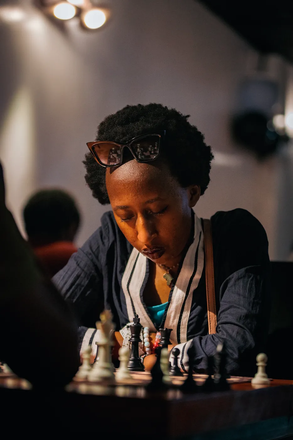 A player with sunglasses pushed up on her head and a striped scarf focuses under warm lights