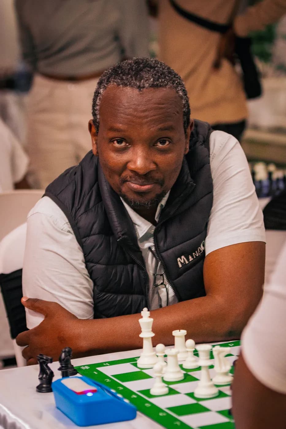 A player in a navy gilet over a white tee looks up from a green and white tournament board
